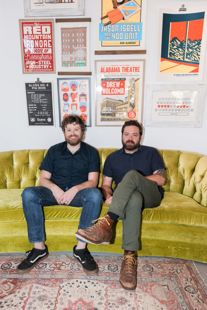 Yellow Hammer Creative's owners Brett Forsyth and Brandon Watkins sitting on couch in front of multiple YHC original posters.