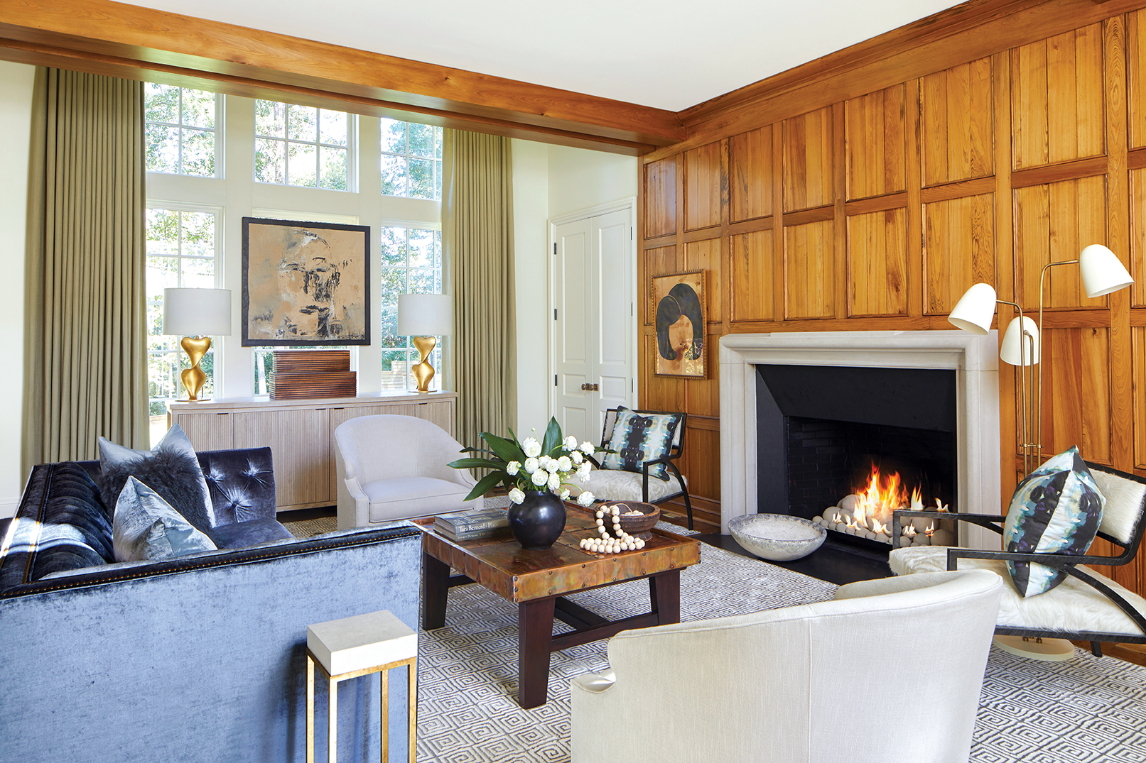 Living room filled with eclectic decor, a wood paneled feature wall and fire place, and blue velvet couch.