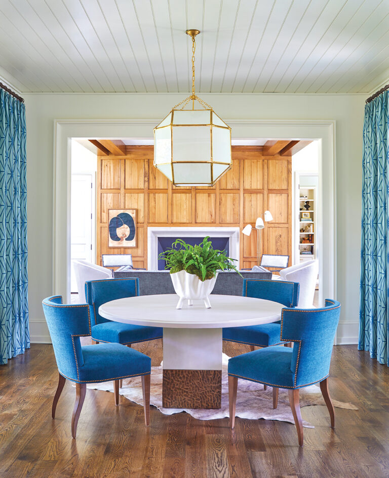 Dining room with round marble table and blue dining chairs onlooking the family room.