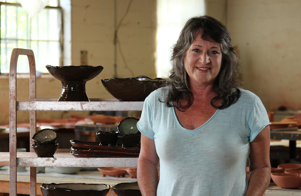 Tena Payne smiling in front of a shelf of finished pottery.