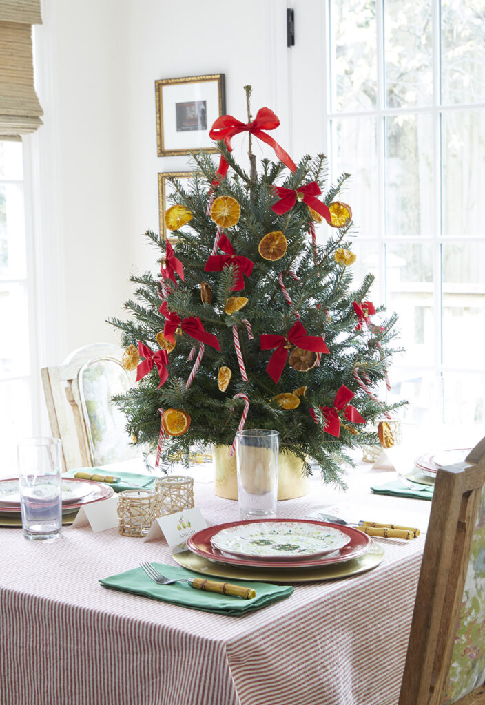 A small Christmas tree on top of a small table is decorated with orange slices, candy canes, and red bows.