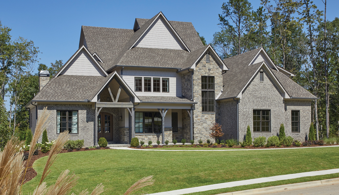 Front exterior elevation photo of large grey home with multiple windows.