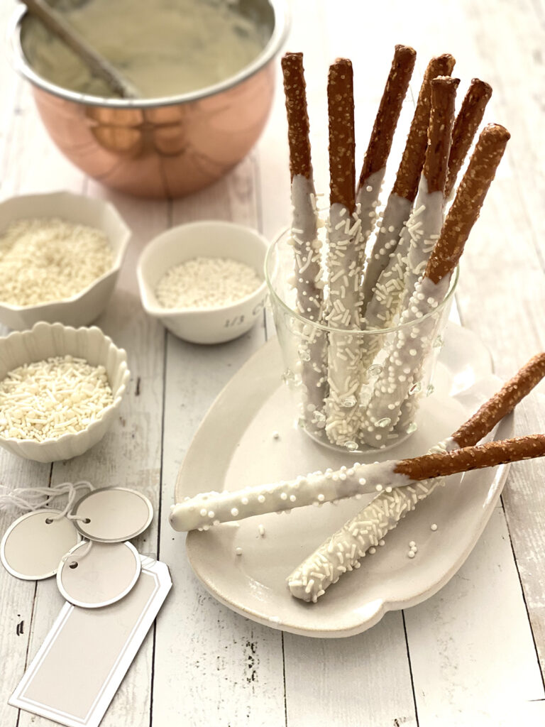 Pretzel sticks dipped in white chocolate styled in a glass cup.