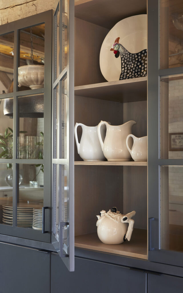 pitchers, painted plates, and other kitchen ware styled in a black cabinet with glass paned door.