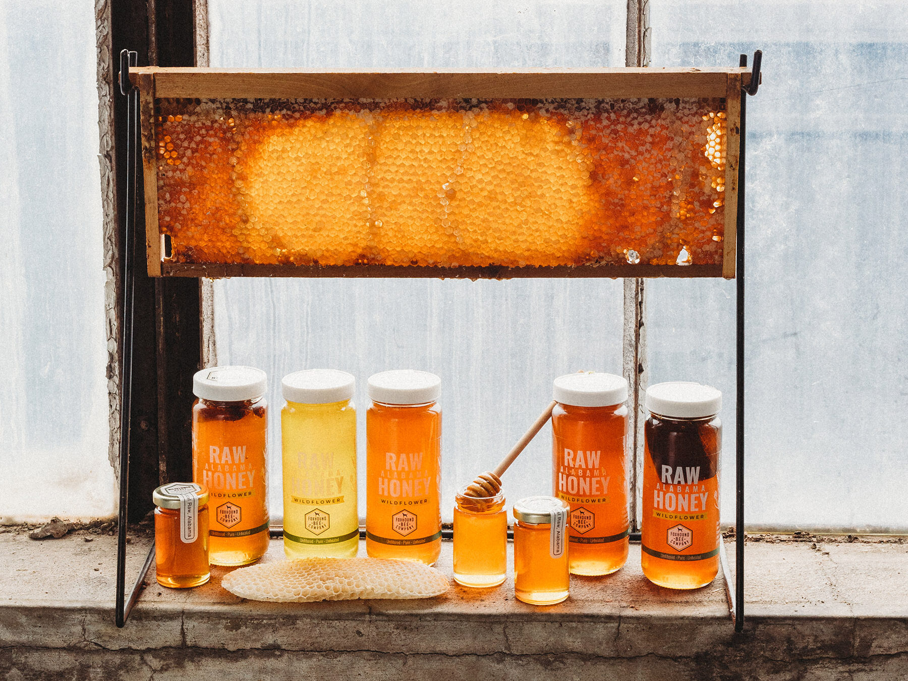 Jars of Fox Hound Bee Company honey below honeycomb on a stand.