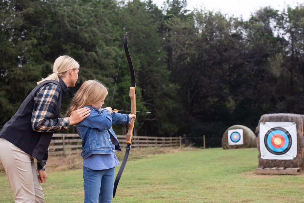 Woman helping young girl learn archery.