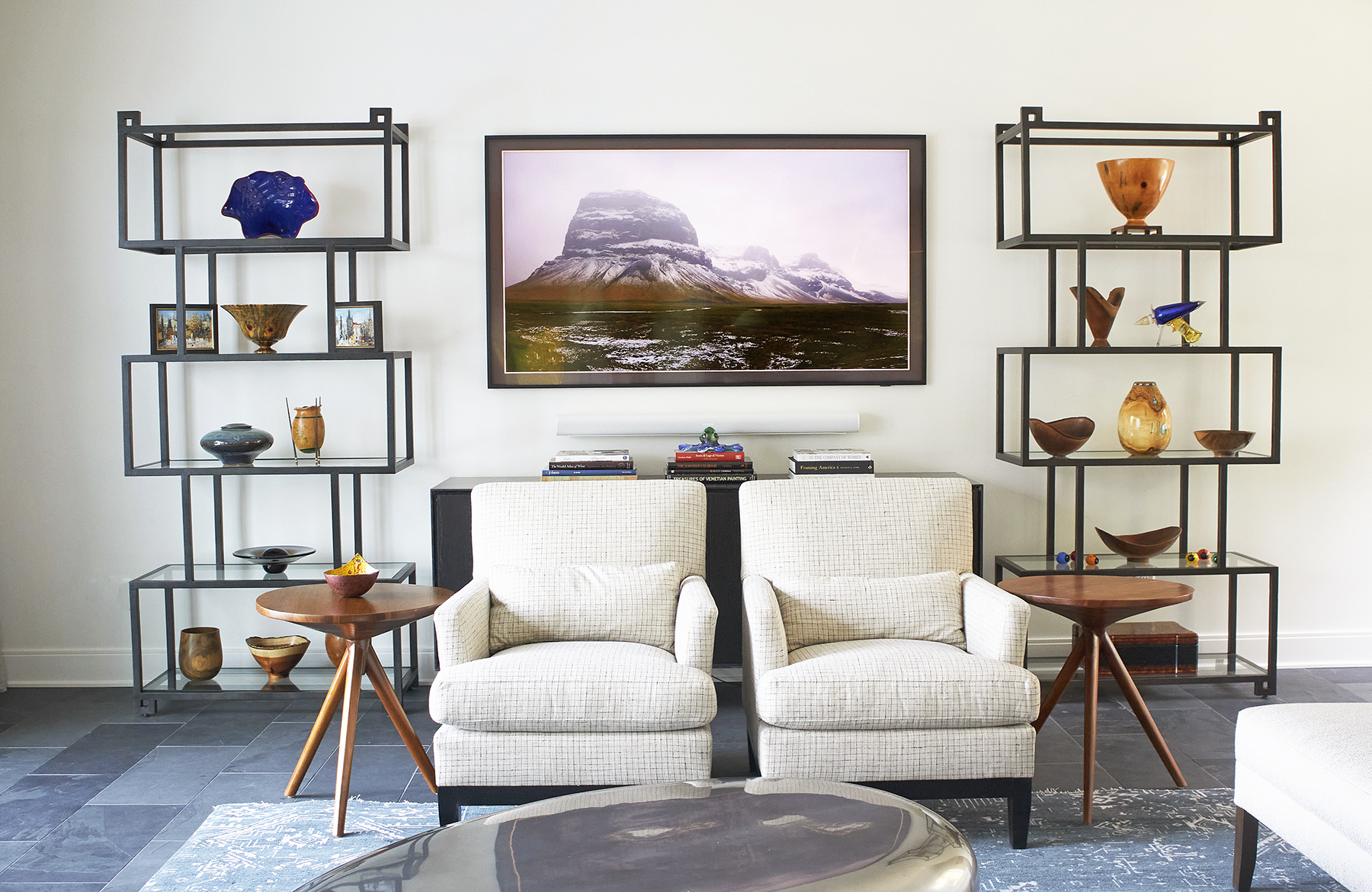 To one side of the living room sits two large shelves filled with pieces from the home owners art collection and separated by a large framed photograph.