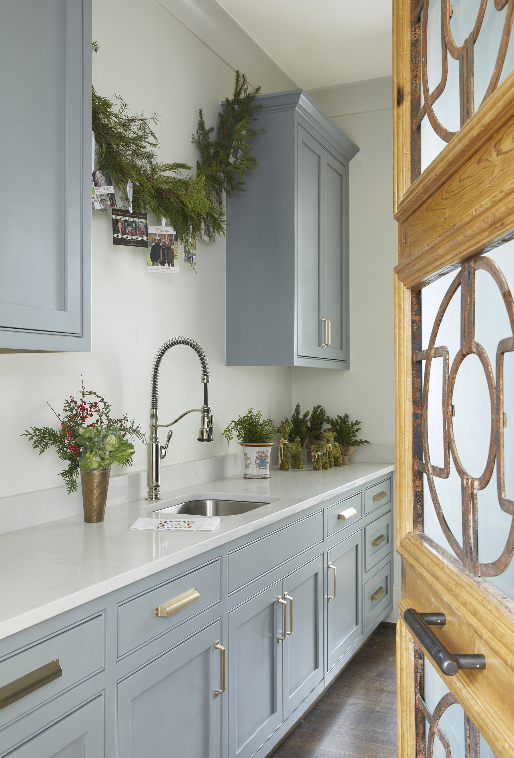 A vintage door opens to the laundry. The cabinets are painted a custom blue-gray color and feature the same quartz countertops as the kitchen.