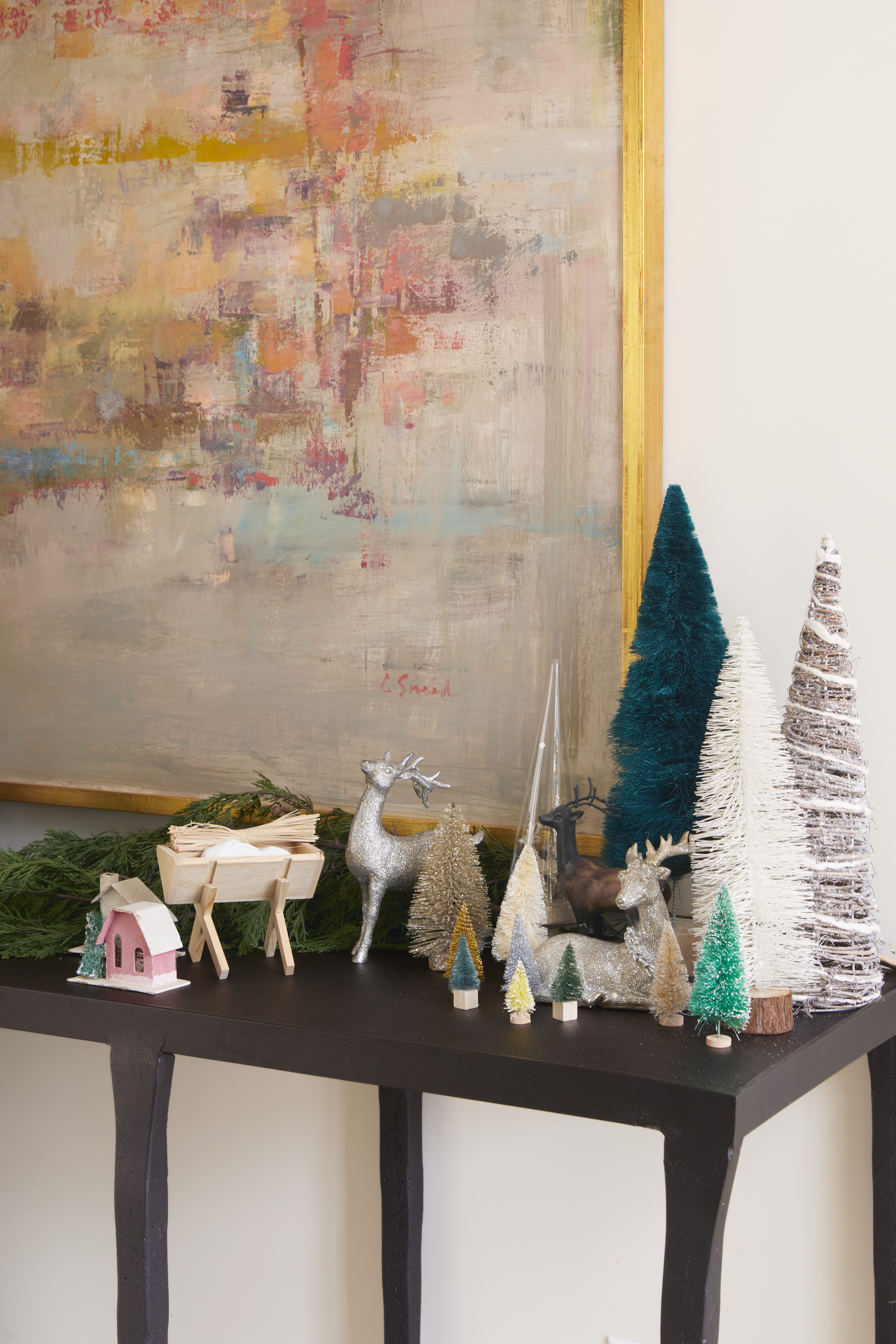 Bottle brush Christmas trees and garland adorn a small table under Carol Sneed Painting.