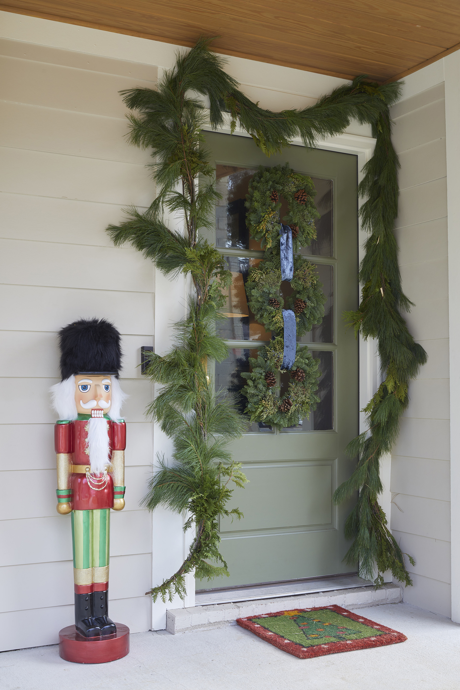 Three wreaths looped together with blue velvet ribbon hung on the front door surrounded by a swag of garland.