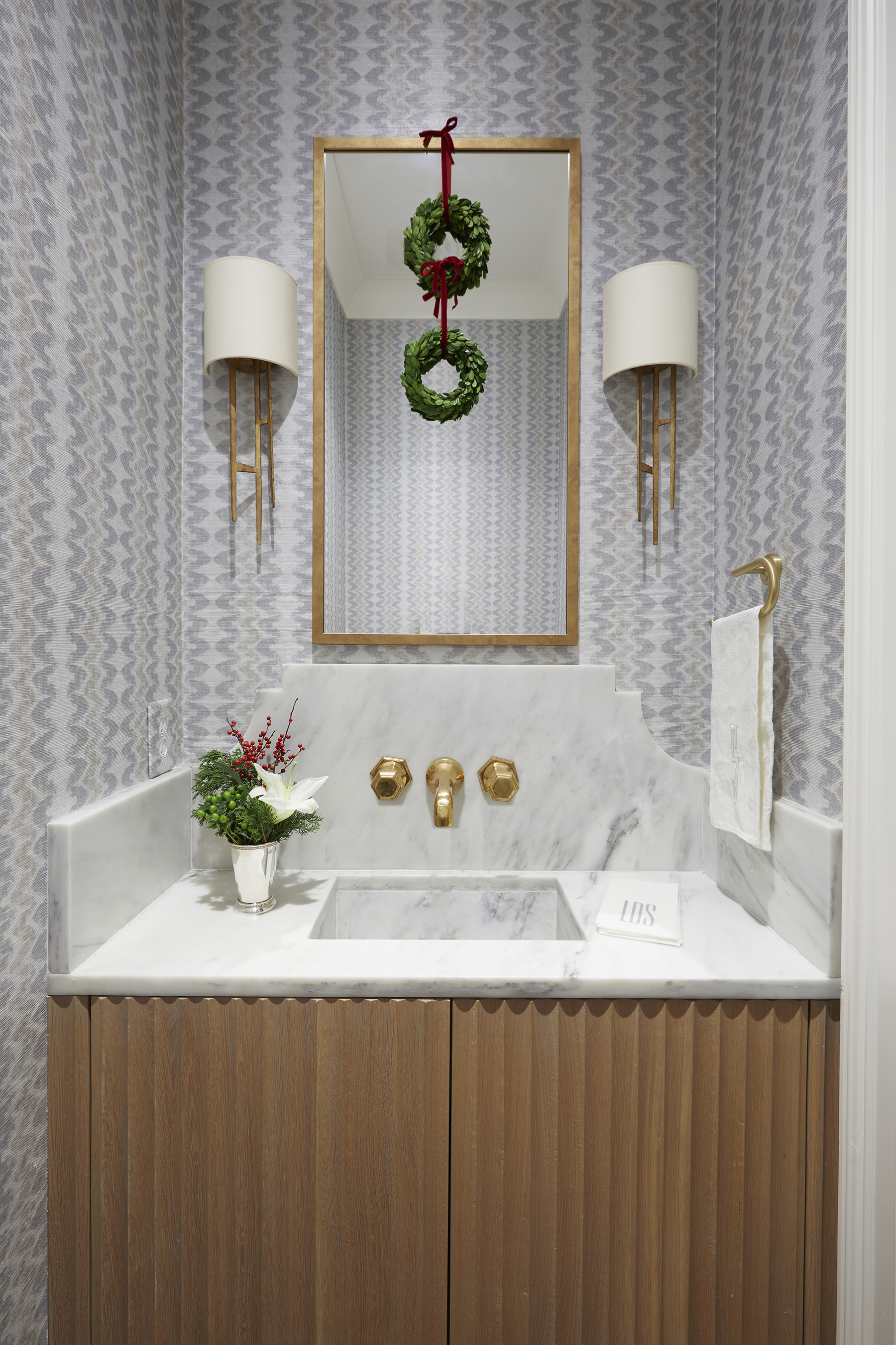 Cowtan and Tout wallpaper shines in a guest bathroom. The hammered gold mirror, gold sconces, and gold faucet finish out the jewel box feel.